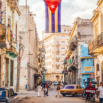Callejón de La Habana, colorido, con carros viejos y la bandera cubana.