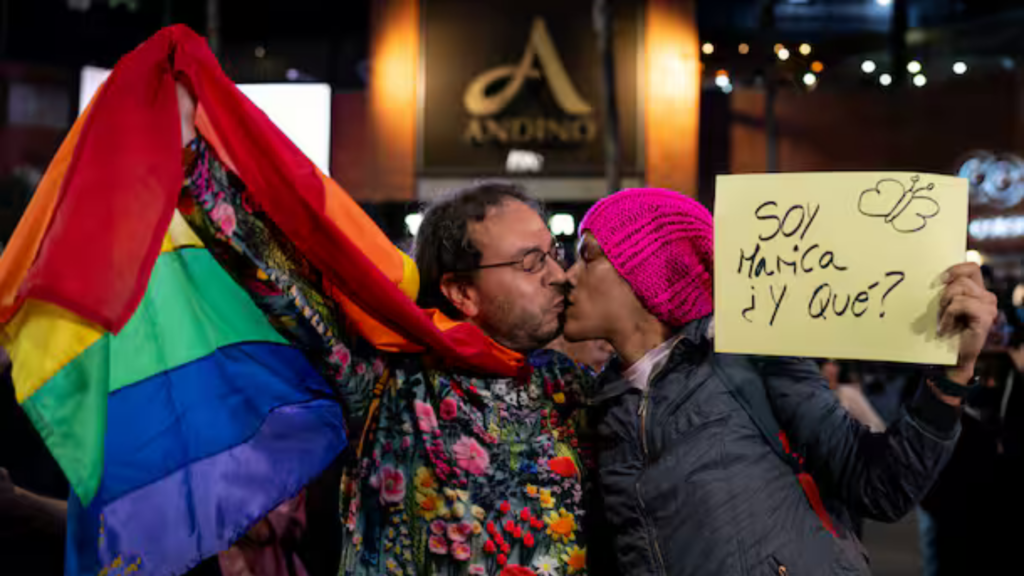 Imagen de dos hombres besándose, con la bandera gay