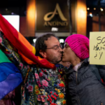 Imagen de dos hombres besándose, con la bandera gay