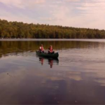 Una canoa con dos personas. El agua se ve en calma.