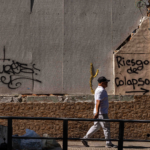 Transeúnte caminando frente a un muro que dice "riesgo de colapso"