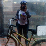 En la foto se ve a Yenny de pie tomándo una selfie mientras sostiene su bicicleta. Tiene puesta la camiseta con una paloma de origami de colores y con la palabra Sí, a favor del plebiscito de 2016 por la paz.