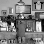 Foto del Bar Las Heras en el que se ven mesas, el mostrador, y una persona dando la espalda. Asumimos que es uno de los personajes mencionados en el texto.