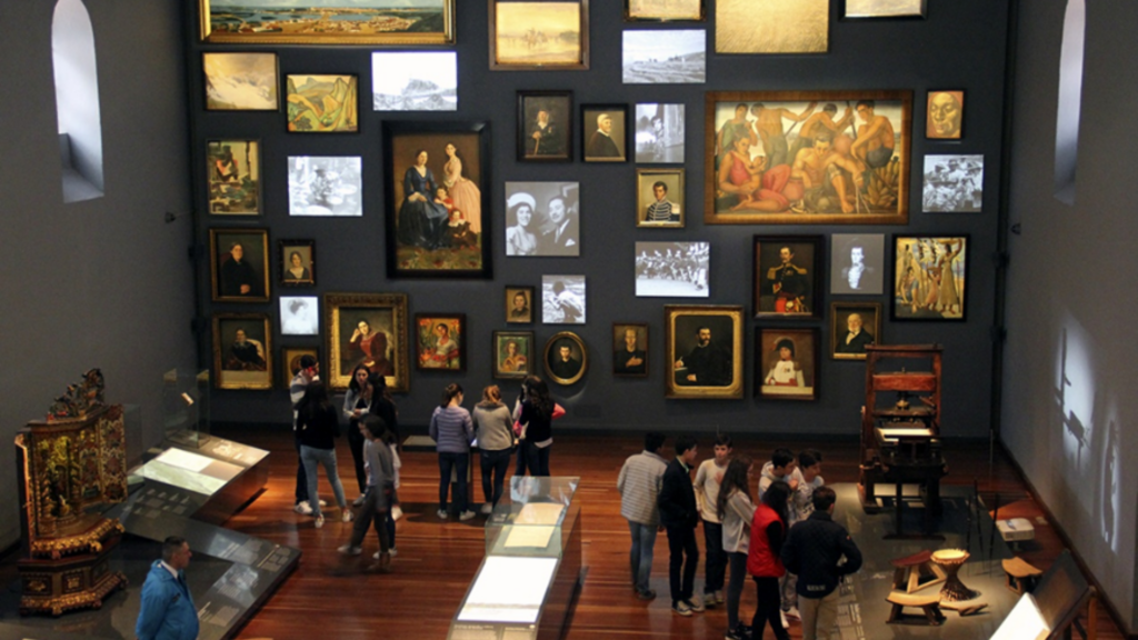 Foto panorámica de la Sala Memoria y nación del Museo Nacional de Colombia en la que se ven varios objetos colagos de la pared y muchas personas visitando el sitio.