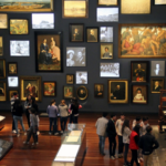 Foto panorámica de la Sala Memoria y nación del Museo Nacional de Colombia en la que se ven varios objetos colagos de la pared y muchas personas visitando el sitio.