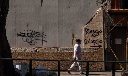 Transeúnte caminando frente a un muro que dice "riesgo de colapso"