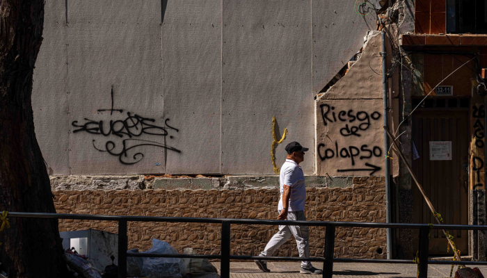 Transeúnte caminando frente a un muro que dice "riesgo de colapso"