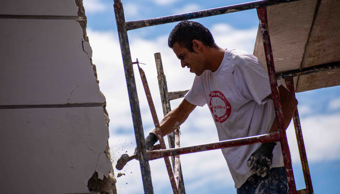 Un hombre golpea la fachada de un edificio de la plaza de Bolivar para desprender los pedazos afectados.