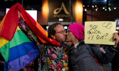 Imagen de dos hombres besándose, con la bandera gay