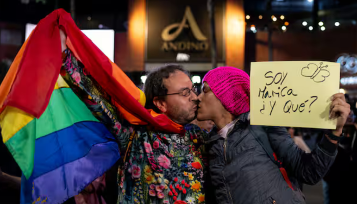 Imagen de dos hombres besándose, con la bandera gay