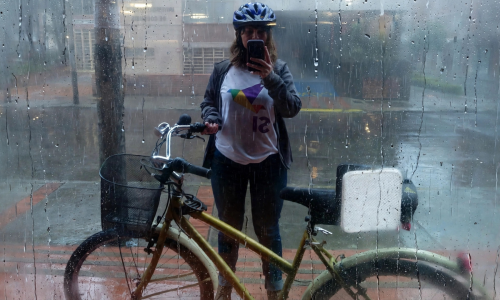 En la foto se ve a Yenny de pie tomándo una selfie mientras sostiene su bicicleta. Tiene puesta la camiseta con una paloma de origami de colores y con la palabra Sí, a favor del plebiscito de 2016 por la paz.