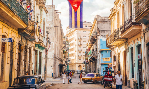 Callejón de La Habana, colorido, con carros viejos y la bandera cubana.